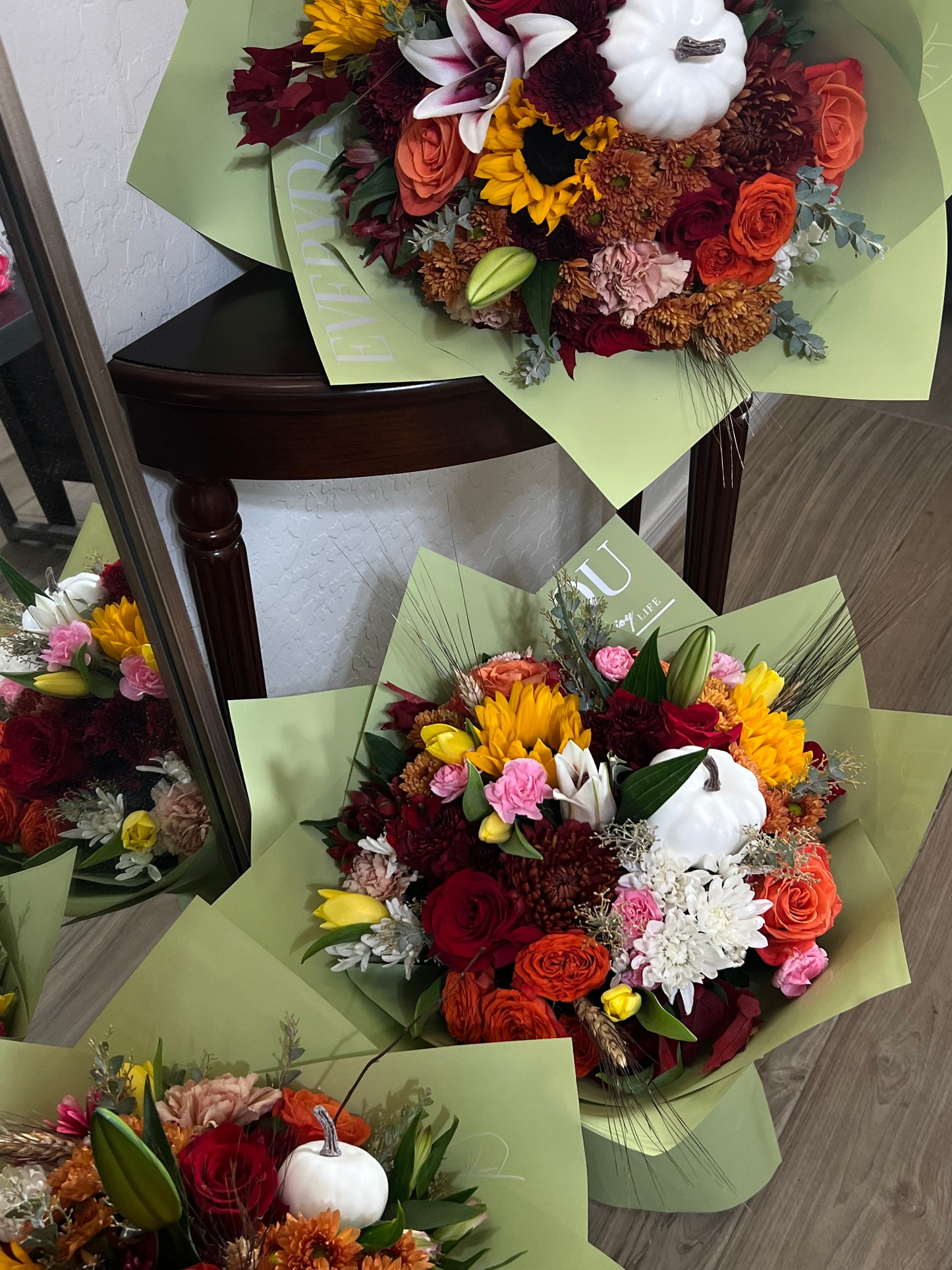 Stunning autumn flower arrangement with vibrant orange roses, deep red dahlias, golden sunflowers, and seasonal greenery, perfect for fall weddings, Thanksgiving centerpieces, and cozy home décor.