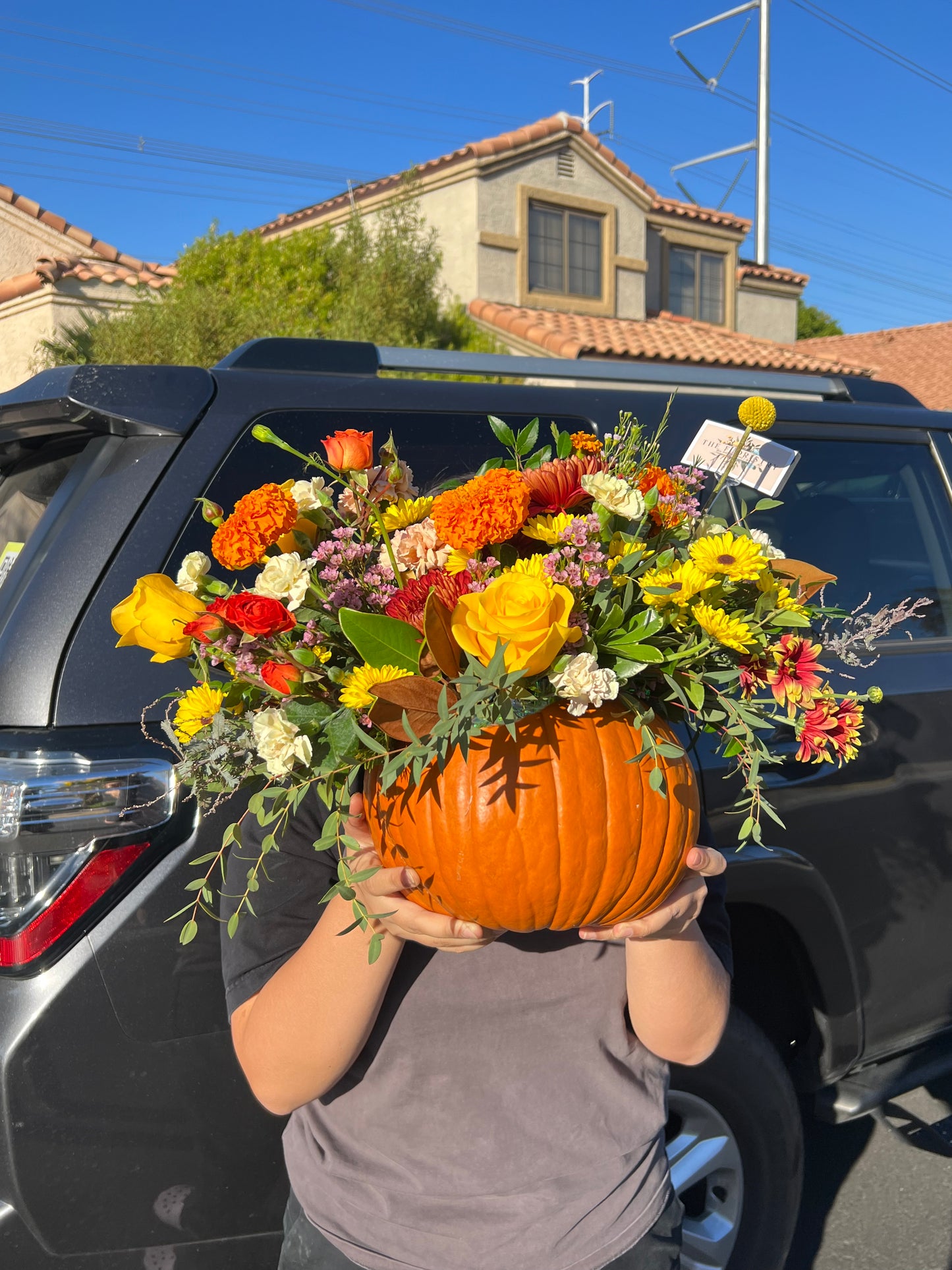 "Surprised Pumpkin Centerpiece featuring fresh flowers and preserved decorations arranged inside a unique pumpkin. Available in standard, deluxe, and premium sizes with varying flower stems and higher-value blooms."
