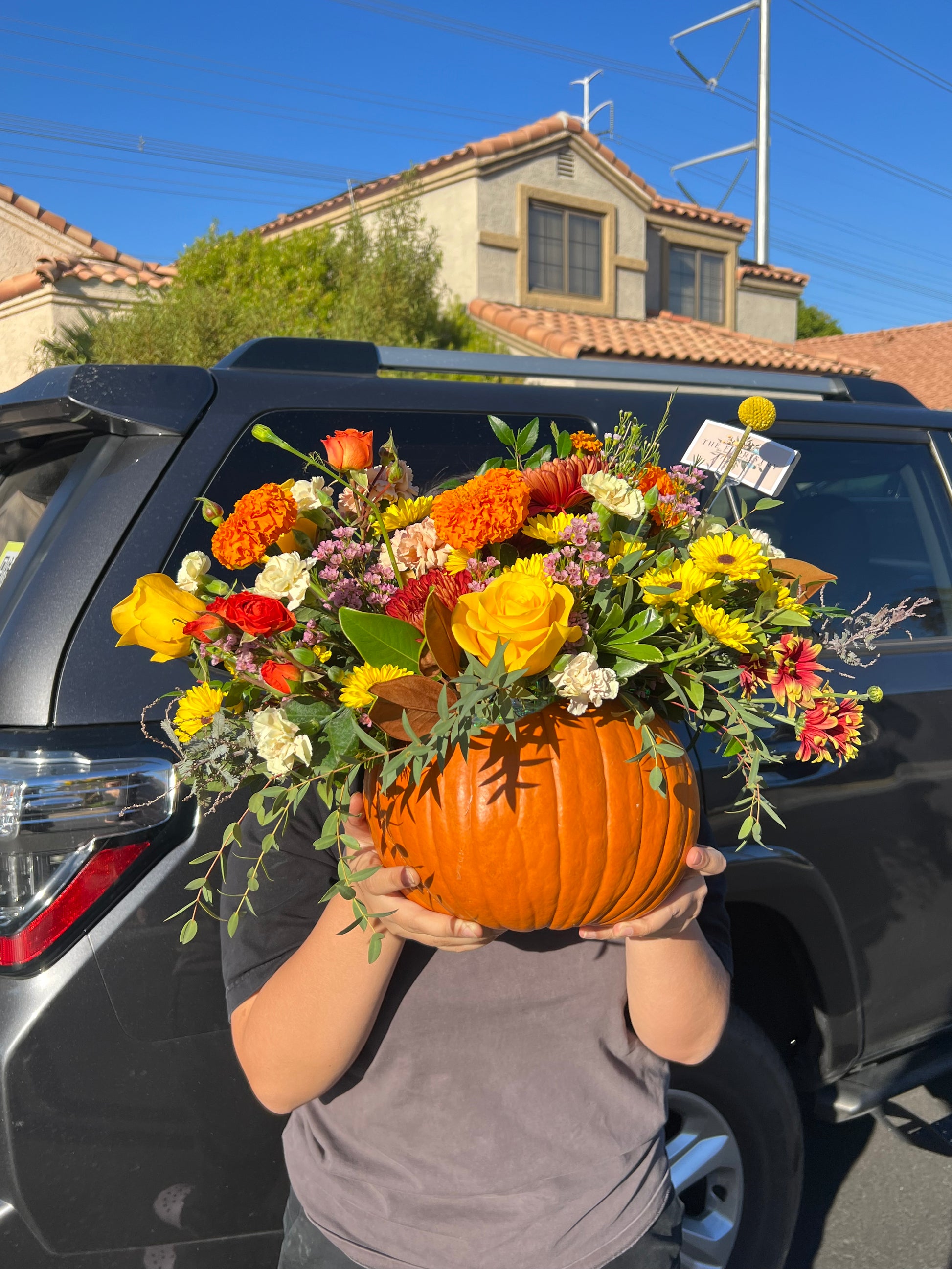 "Surprised Pumpkin Centerpiece featuring fresh flowers and preserved decorations arranged inside a unique pumpkin. Available in standard, deluxe, and premium sizes with varying flower stems and higher-value blooms."
