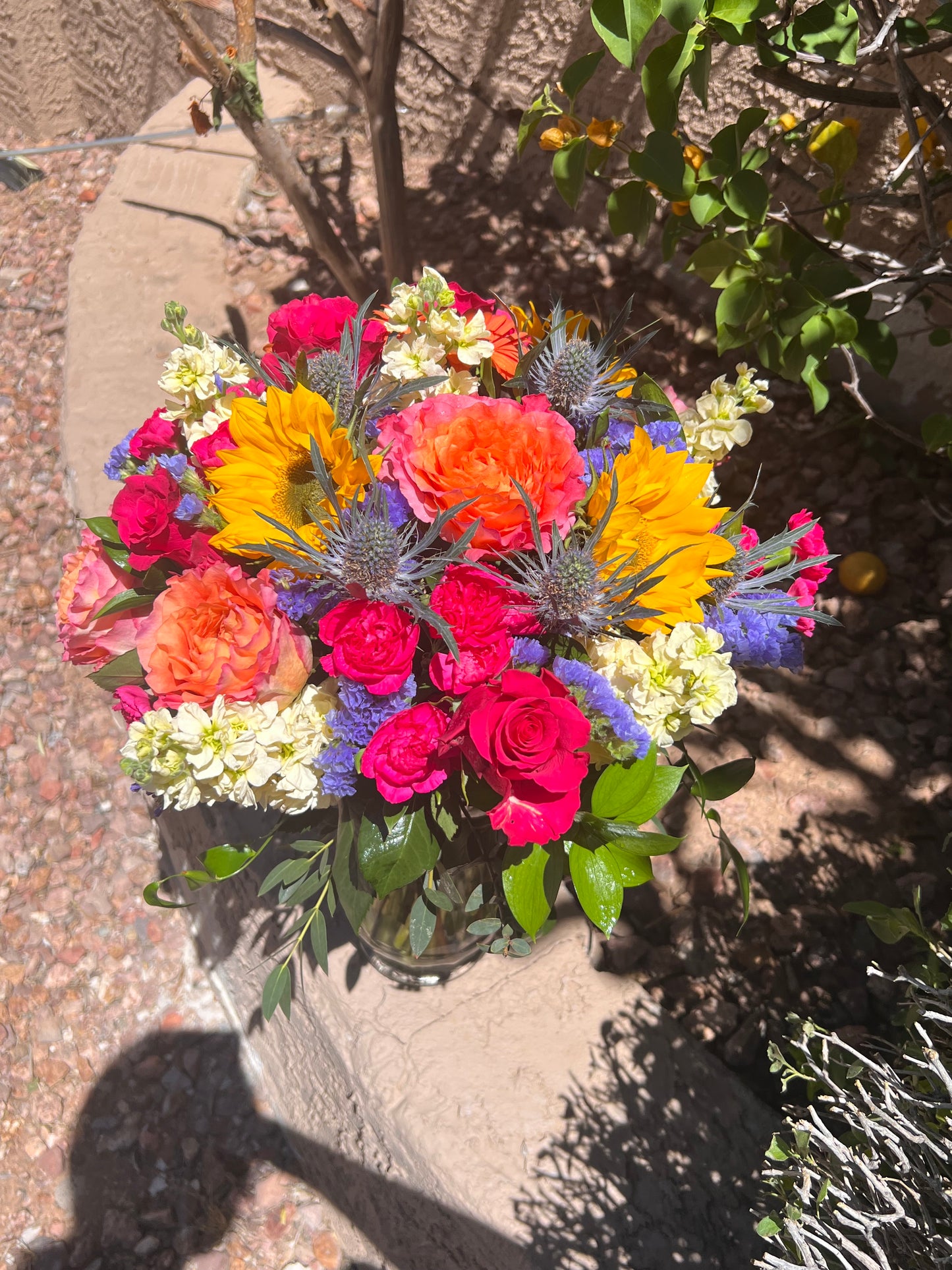 Colorful bouquet with hot pink, violet, yellow, lavender, and peach blooms arranged with seasonal greenery.
