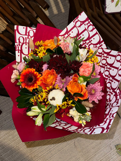 Fall bouquet with yellow, orange, red, and brown seasonal blooms, wrapped with filler, greenery, and fall decoration