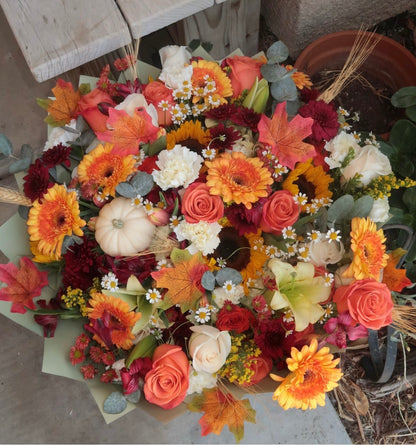 Fall bouquet with yellow, orange, red, and brown seasonal blooms, wrapped with filler, greenery, and fall decoration