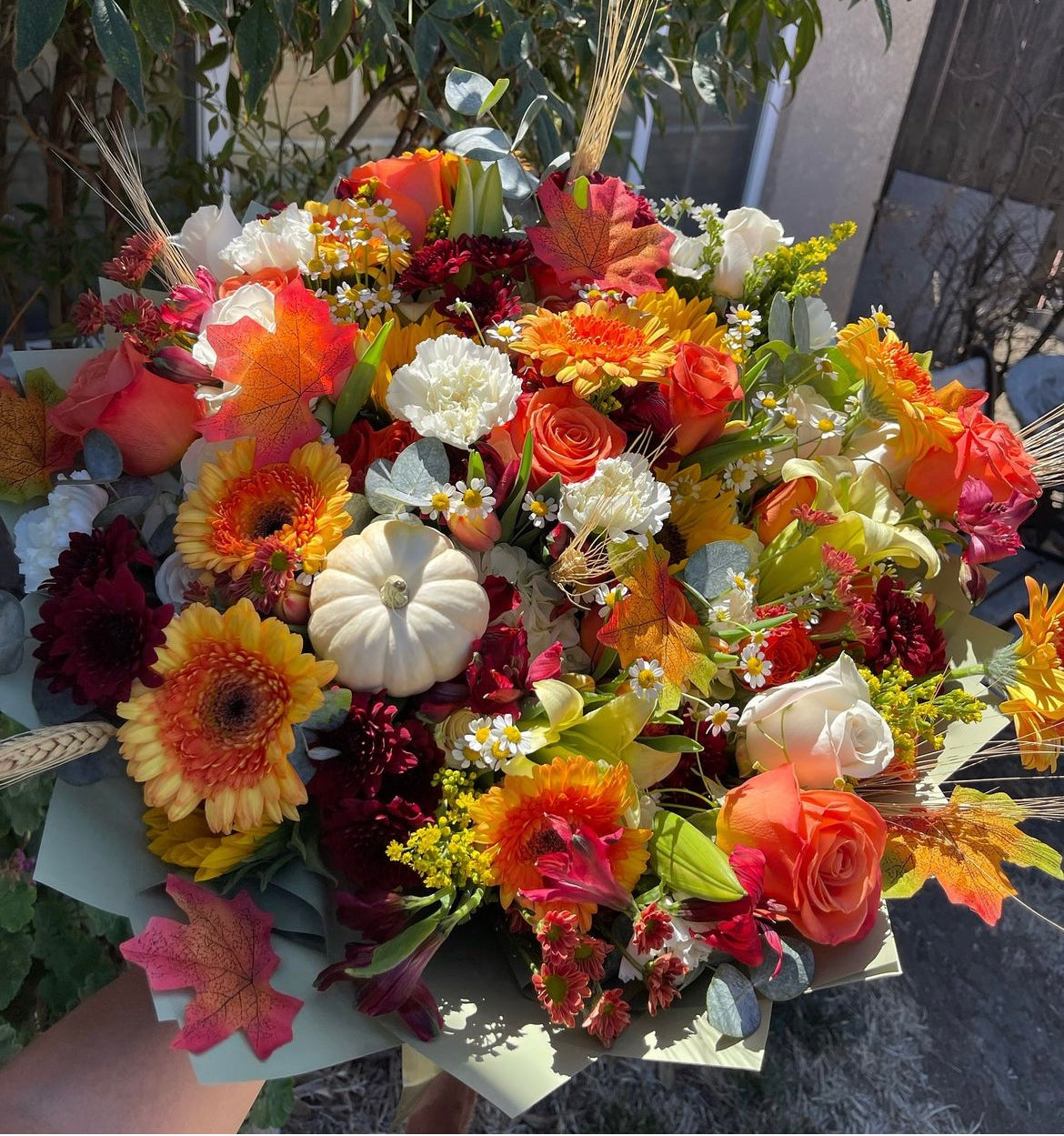 Fall bouquet with yellow, orange, red, and brown seasonal blooms, wrapped with filler, greenery, and fall decoration