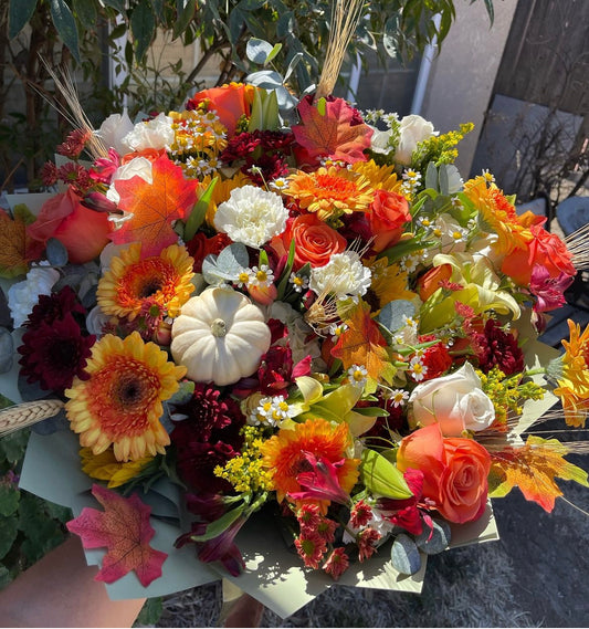 Fall bouquet with yellow, orange, red, and brown seasonal blooms, wrapped with filler, greenery, and fall decoration