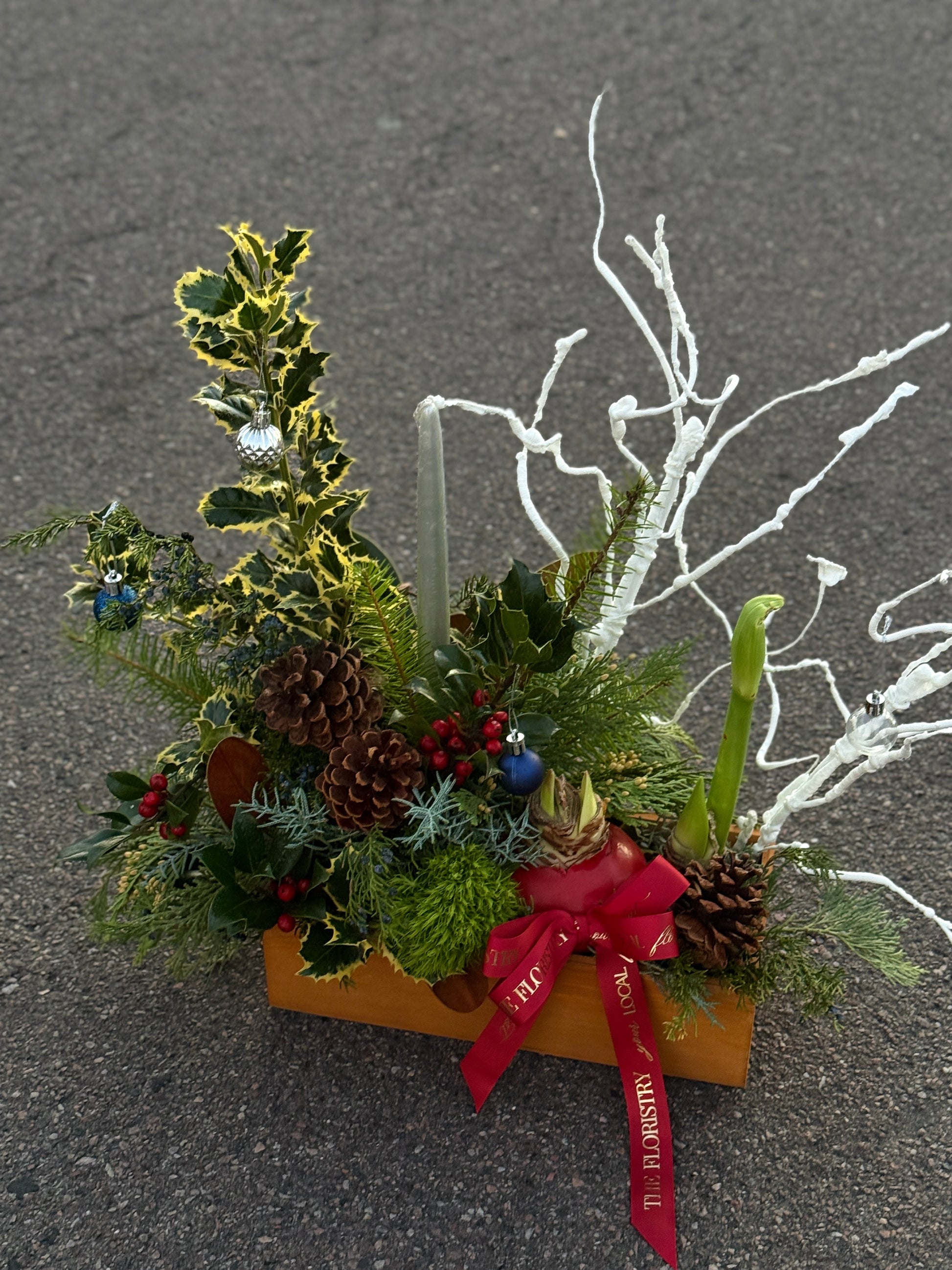 Decorative Christmas arrangement with greenery, pinecones, and a red ribbon delivery in Queen Creek AZ.