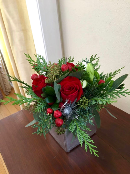 Small crimson holiday centerpiece with red roses, greenery, and ornaments. Perfect for festive tables and seasonal gifting.