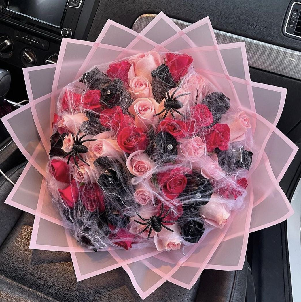 A bouquet of roses with a Halloween theme, featuring a variety of shapes and colors including red and black spider webs, and black and pink roses, presented in a car.