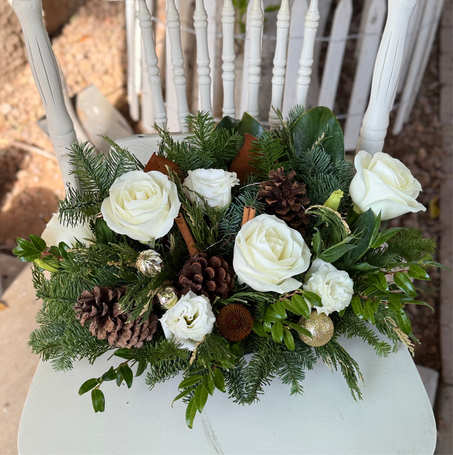 Decorative floral arrangement with white roses, pinecones, and greenery on a white chair.