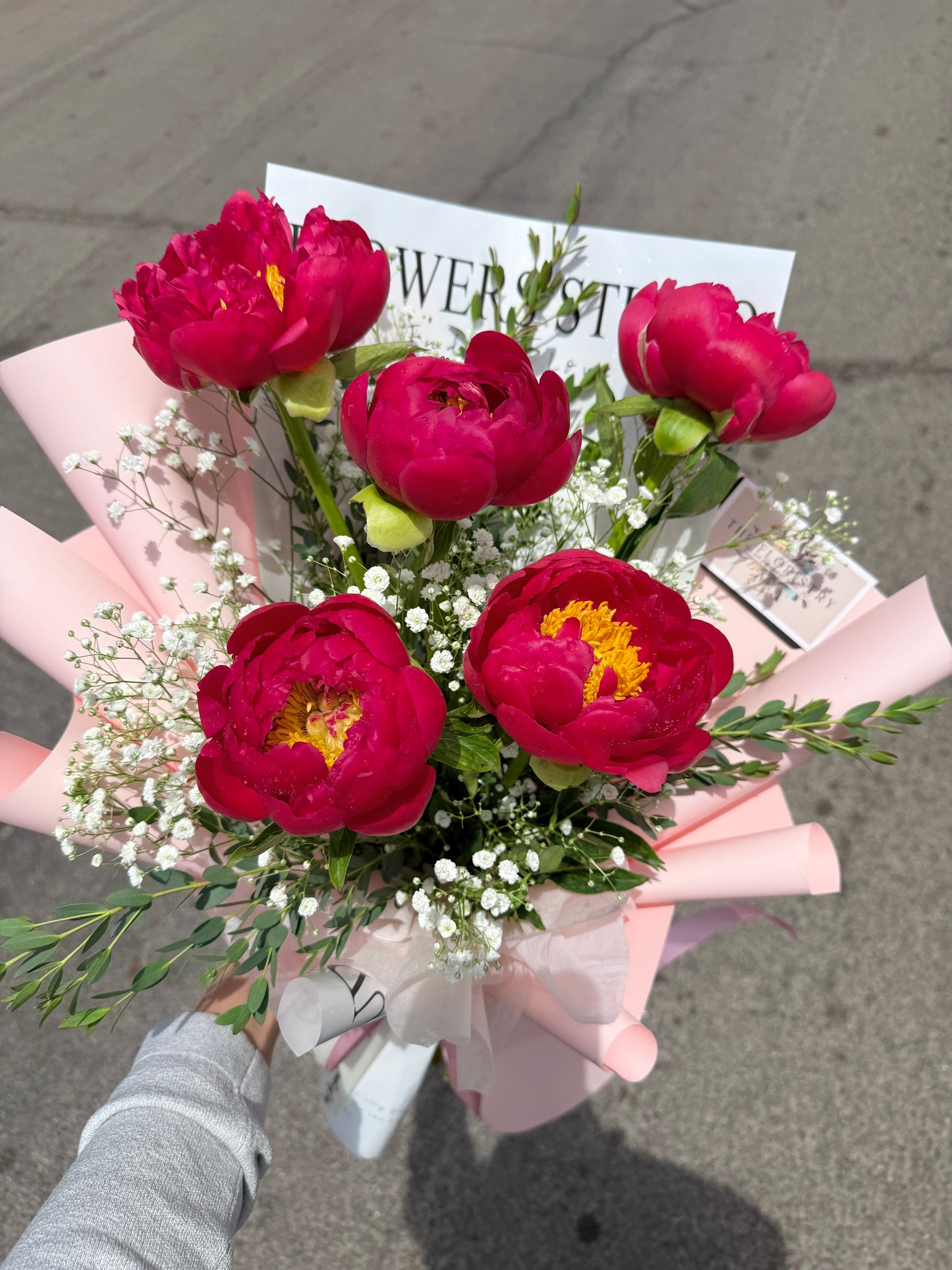 Bouquet of peonies flowers held by a person on a street.
