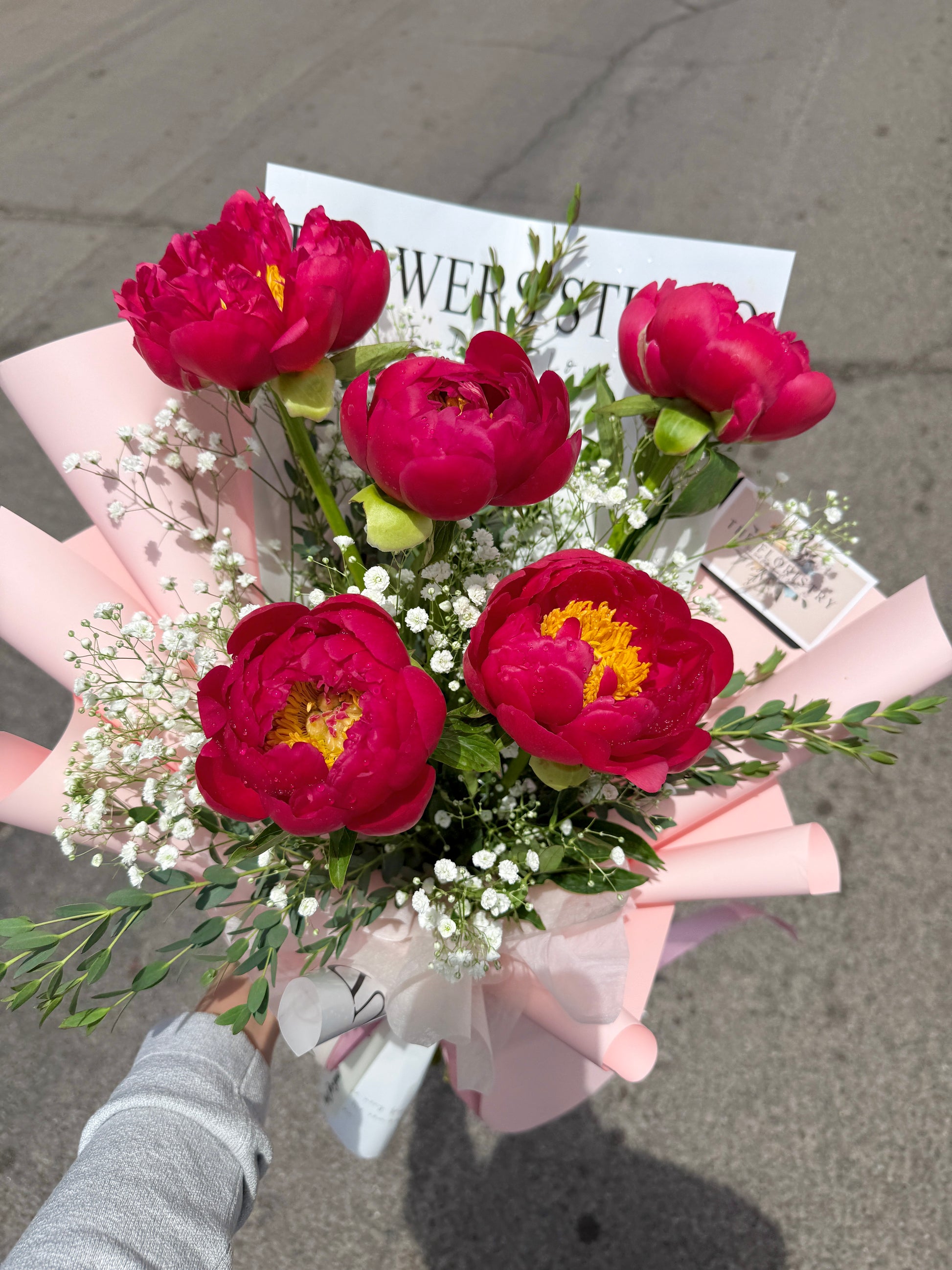 Bouquet of peonies flowers held by a person on a street.