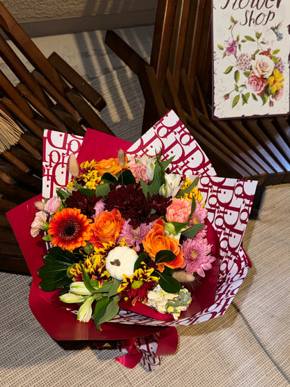 Fall bouquet with yellow, orange, red, and brown seasonal blooms, wrapped with filler, greenery, and fall decoration