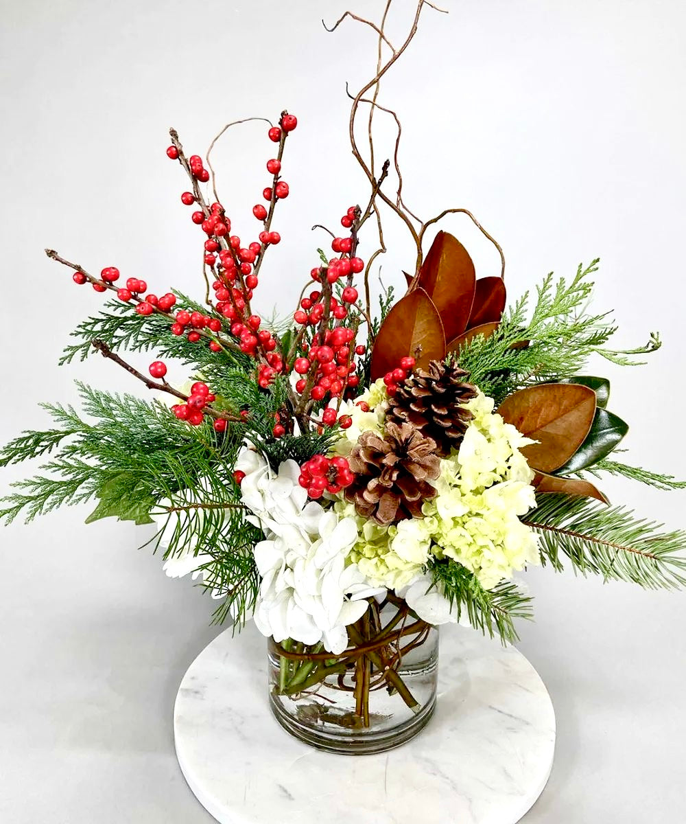  floral arrangement with roses, silvery eucalyptus, woody accents, and lush greenery in Standard, Deluxe, and Premium sizes.
