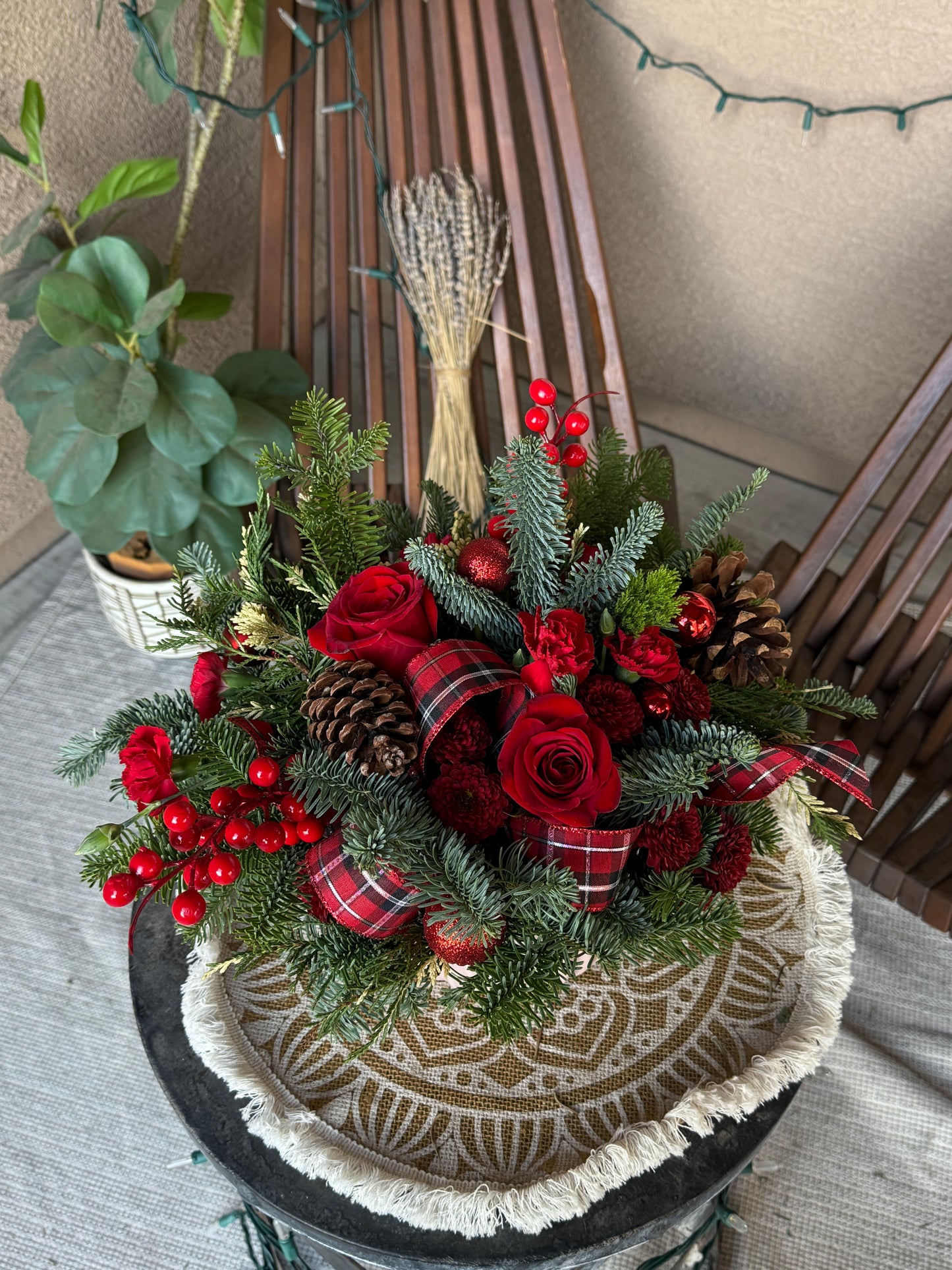 Holiday table centerpiece in red tones featuring fresh winter greenery, pinecones, and seasonal decorations